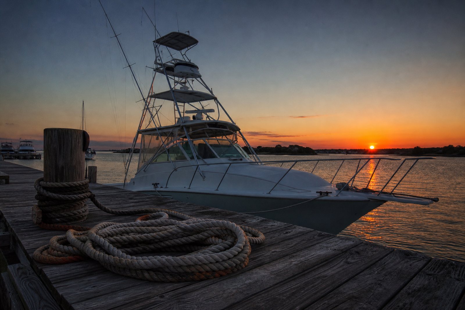 Sport fishing boat tied at a weathered wooden dock at sunrise with calm harbor water and coiled rope on the planks
